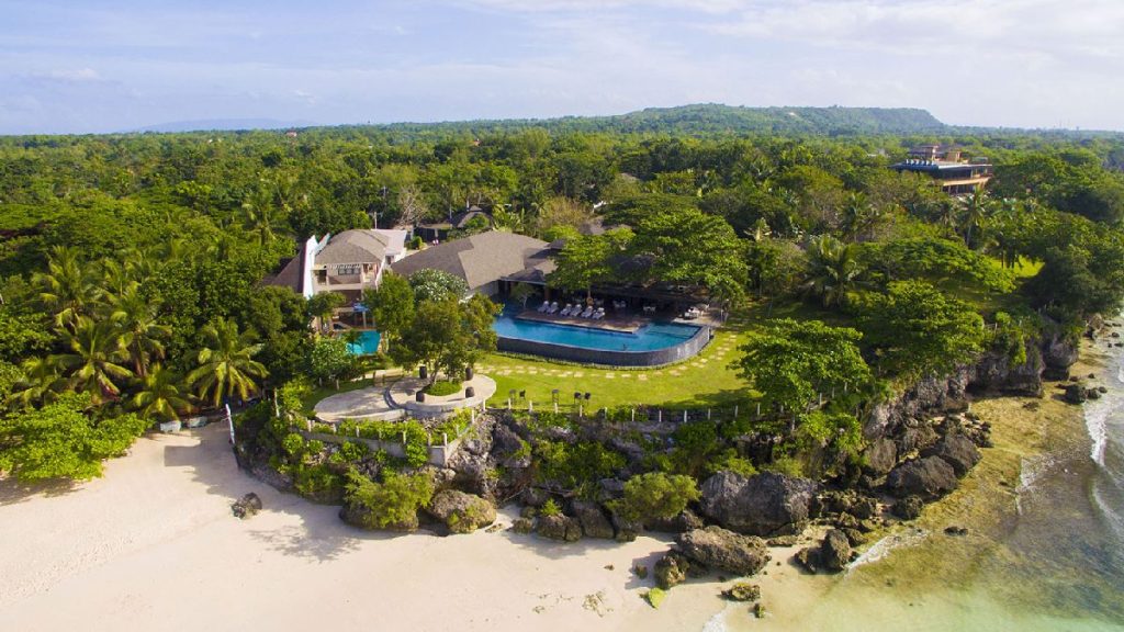 Aerial view of Amorita Resort in Bohol, showing the cliffside infinity pool, lush tropical gardens, and white sand beach along the coastline