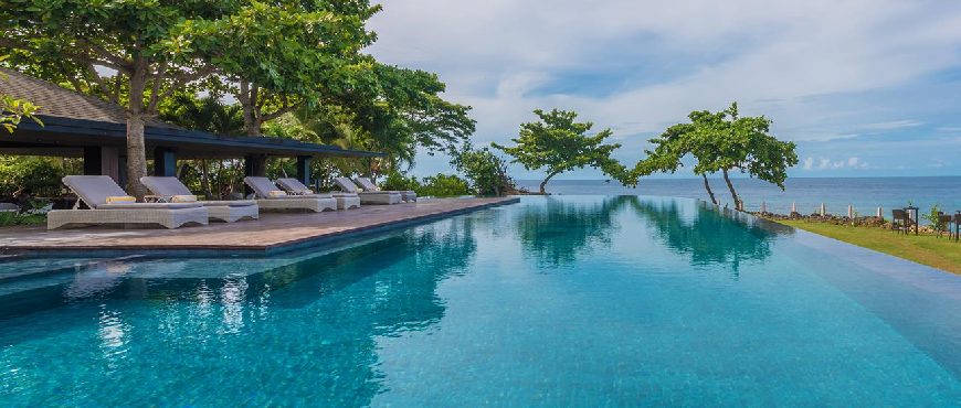 Infinity pool at Amorita Resort in Bohol overlooking the ocean, with lounge chairs, tropical trees, and a clear blue sky
