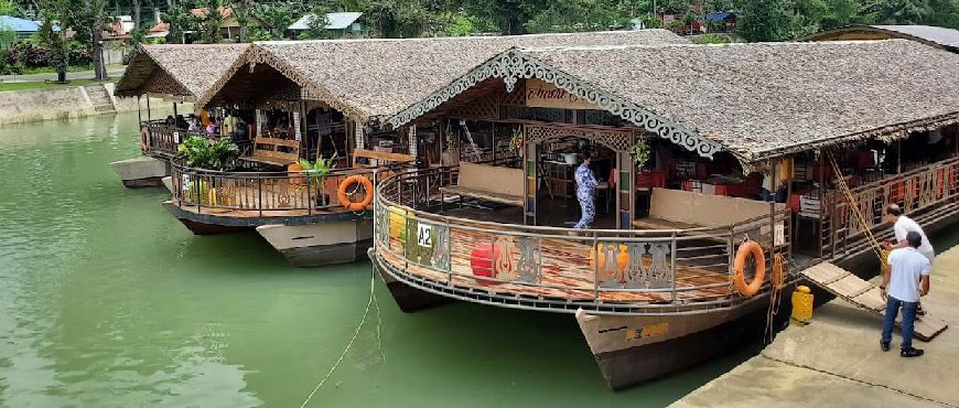 Three traditional wooden floating restaurants moored on the green Loboc River, Bohol, with thatched roofs and life rings.