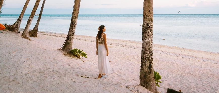 Woman walking along white sand beach in Anda, Bohol with palm trees and calm blue sea.