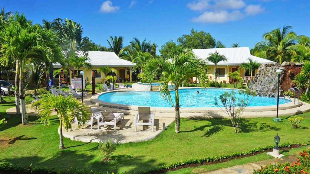 Bohol Sunside Resort swimming pool surrounded by palm trees, lounge chairs, and tropical garden with resort cottages in the background