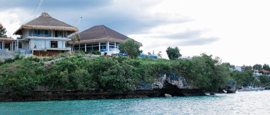 Casa Filomena Resort in Dauis, Bohol overlooking turquoise waters, with nipa-roof buildings on a coastal cliff surrounded by lush greenery