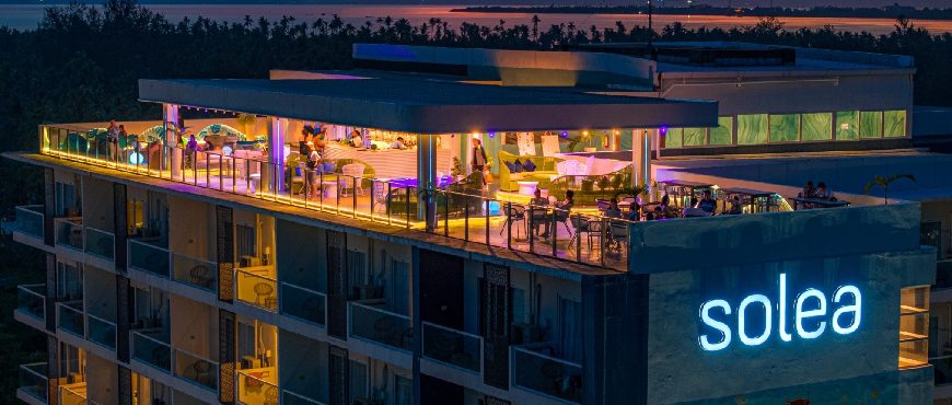 Solea Bohol beachfront resort at dusk, featuring a modern building with illuminated rooftop lounge, outdoor seating, and ocean views.